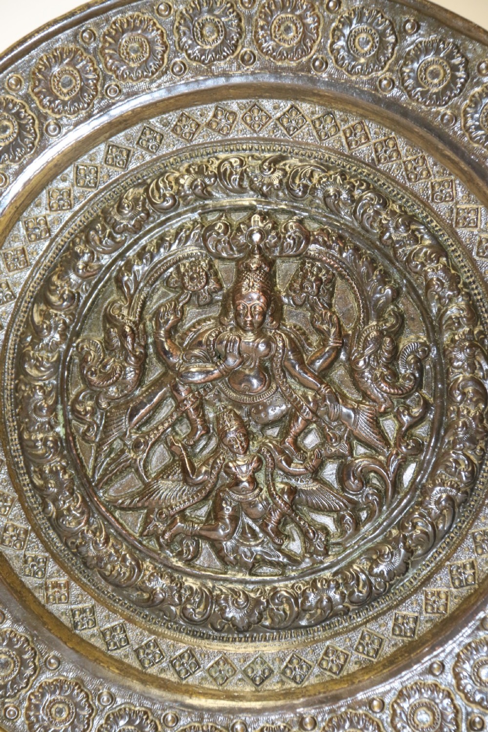 A circular 19th-century Indian bronze plaque featuring intricate chased floral borders and a central high-relief Hindu deity figure. View III