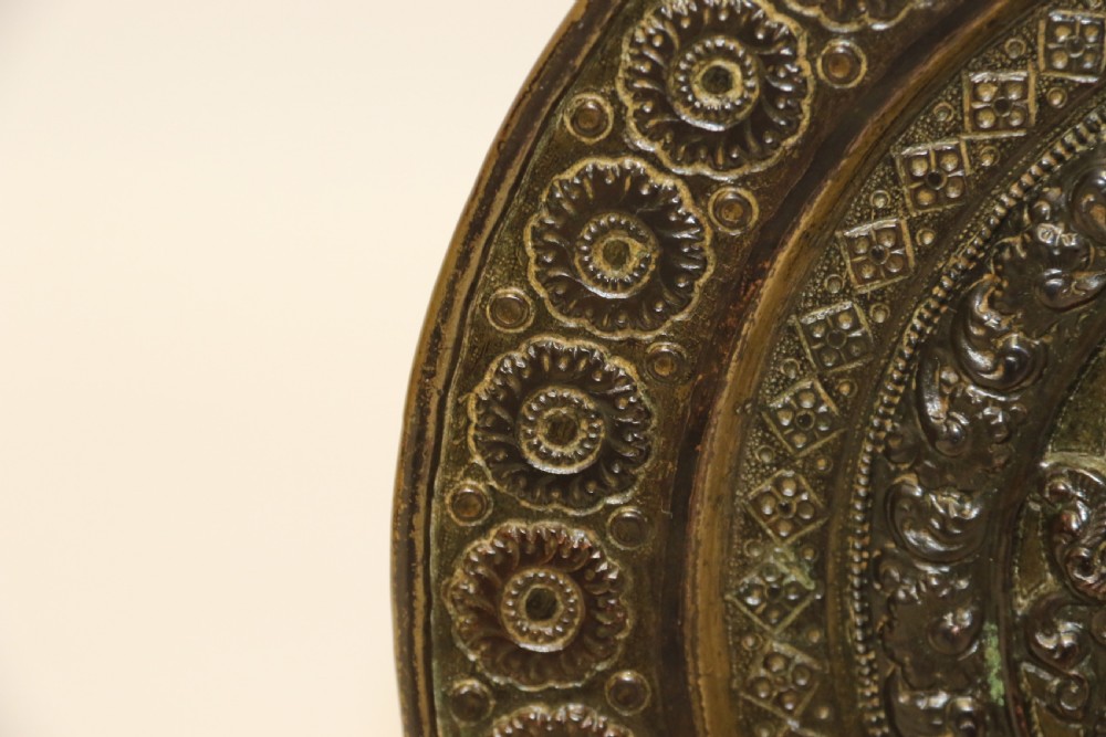 A circular 19th-century Indian bronze plaque featuring intricate chased floral borders and a central high-relief Hindu deity figure. View V