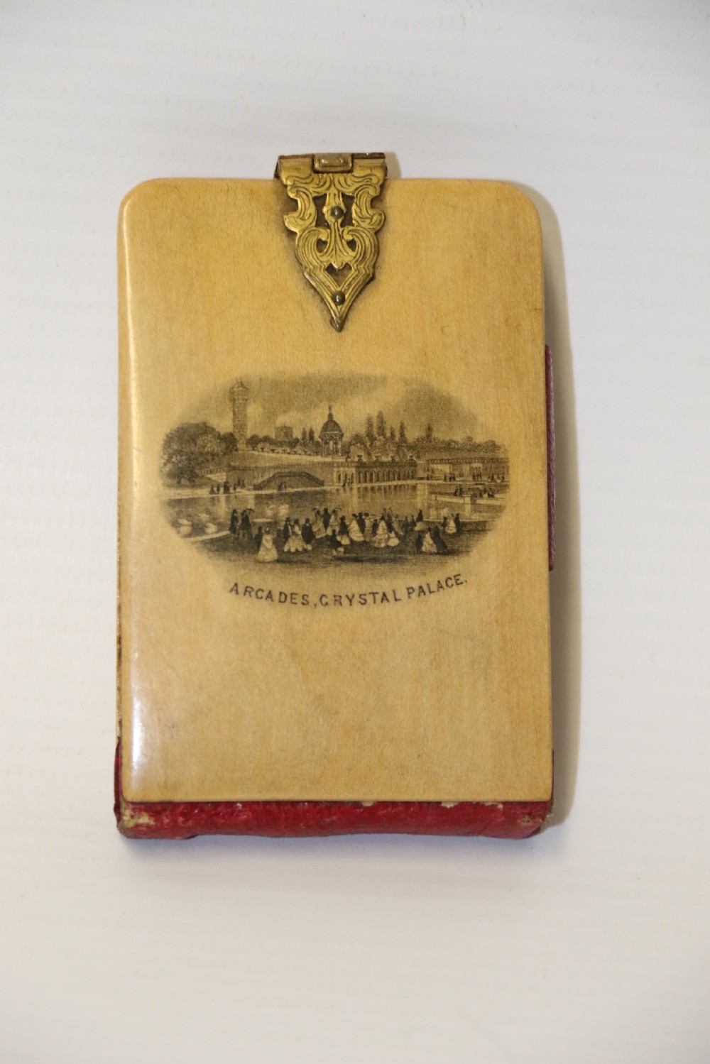 An antique Victorian Mauchline ware wooden pocket notebook displaying a black oval transfer print depicting the Arcades at Crystal Palace, featuring an ornate brass top clasp.