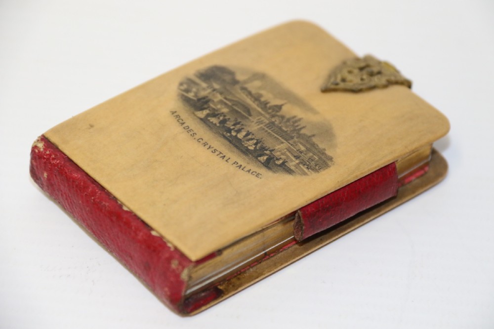 An antique Victorian Mauchline ware wooden pocket notebook displaying a black oval transfer print depicting the Arcades at Crystal Palace, featuring an ornate brass top clasp. View III