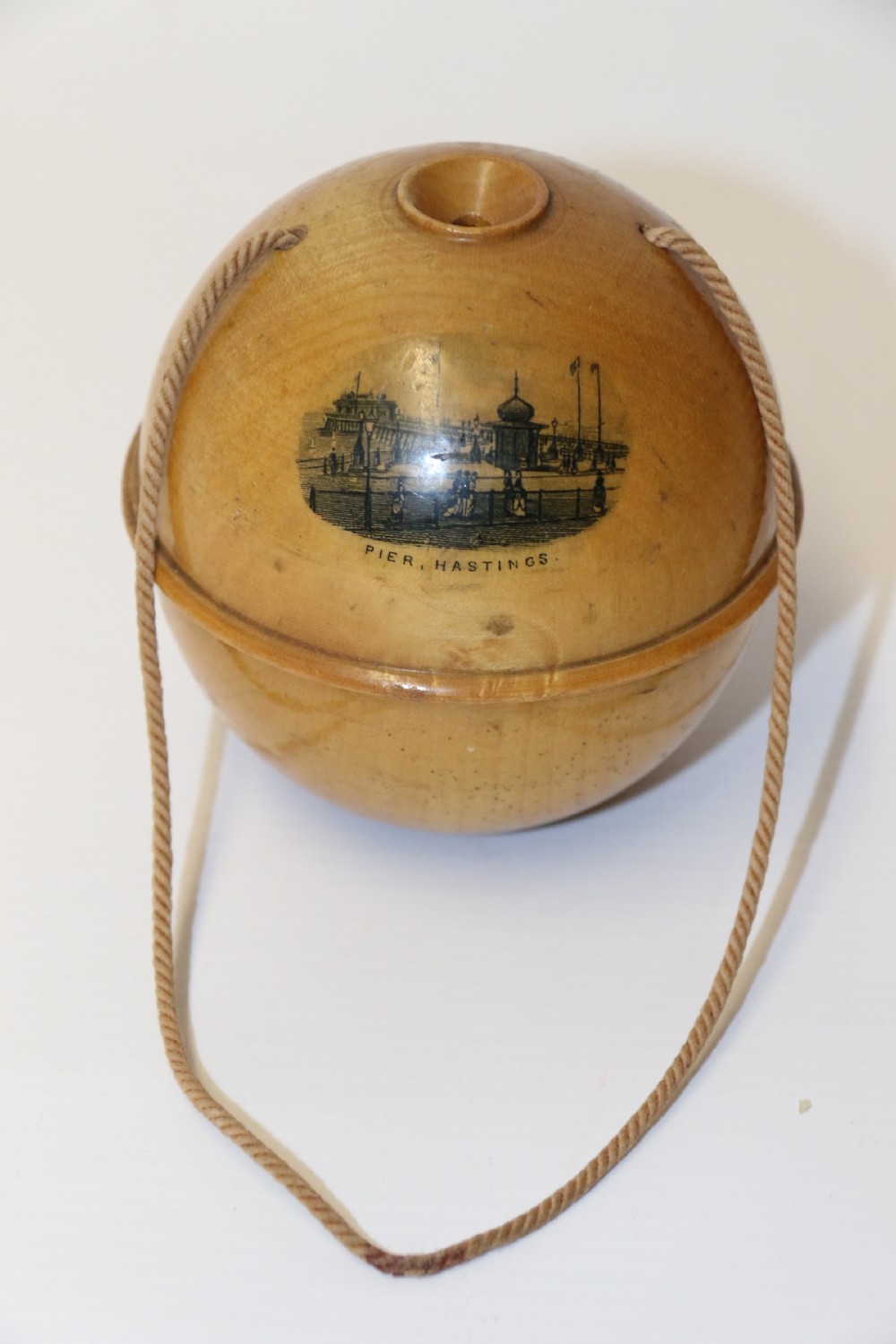 A spherical turned wooden Mauchline ware string holder featuring a black transfer print of Hastings Pier and a hanging cord. View II