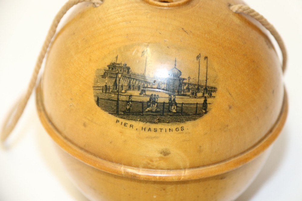A spherical turned wooden Mauchline ware string holder featuring a black transfer print of Hastings Pier and a hanging cord. View IV