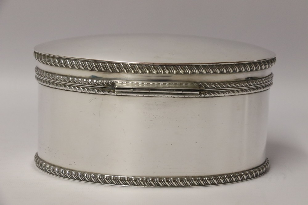 A polished silver-plated oval box featuring a smooth domed lid and rope-twist borders around the rim and base. View III