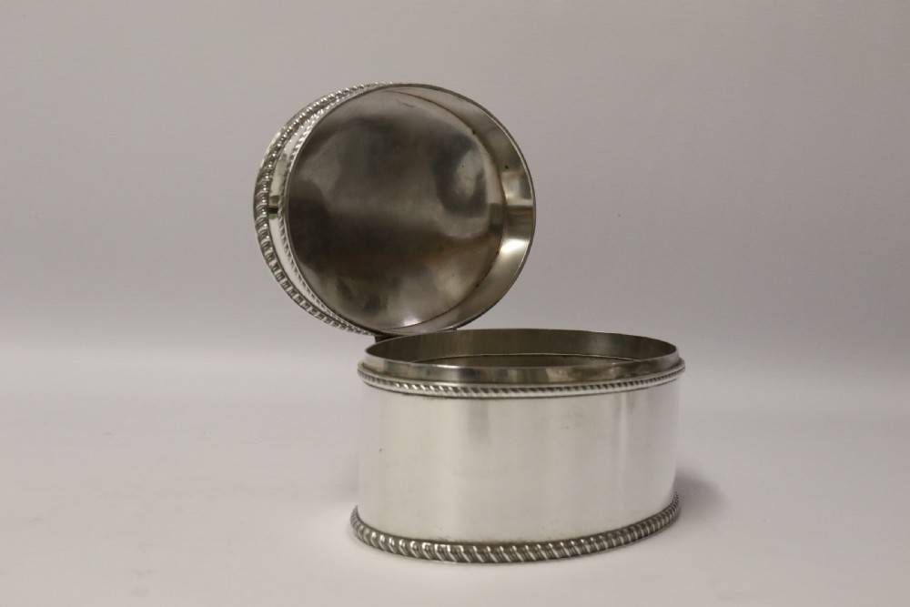 A polished silver-plated oval box featuring a smooth domed lid and rope-twist borders around the rim and base. View VI