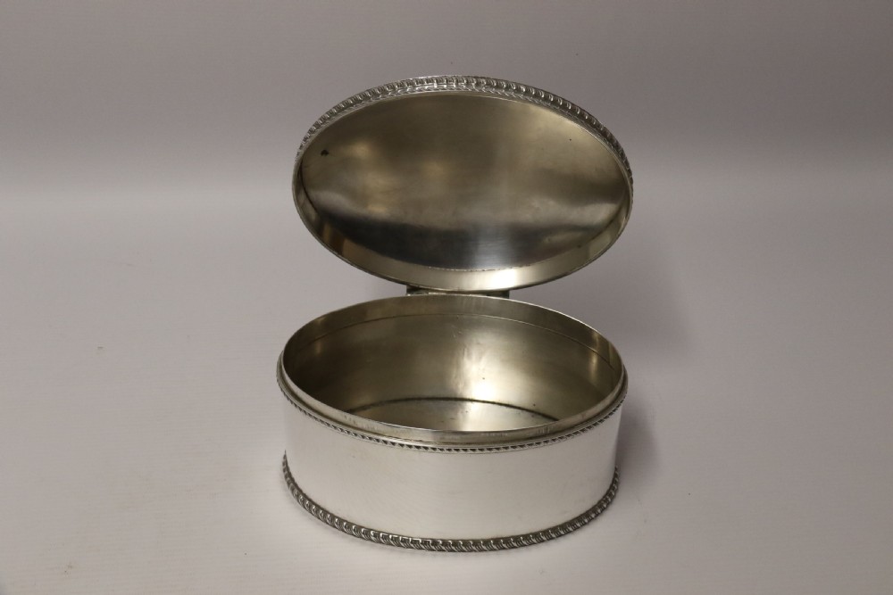 A polished silver-plated oval box featuring a smooth domed lid and rope-twist borders around the rim and base. View VII