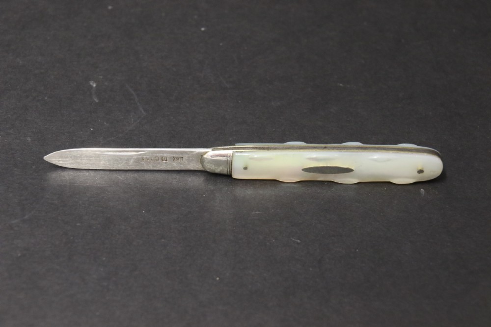 A George V sterling silver folding fruit knife featuring a hallmarked blade and a shaped mother of pearl handle with brass lining. View IV