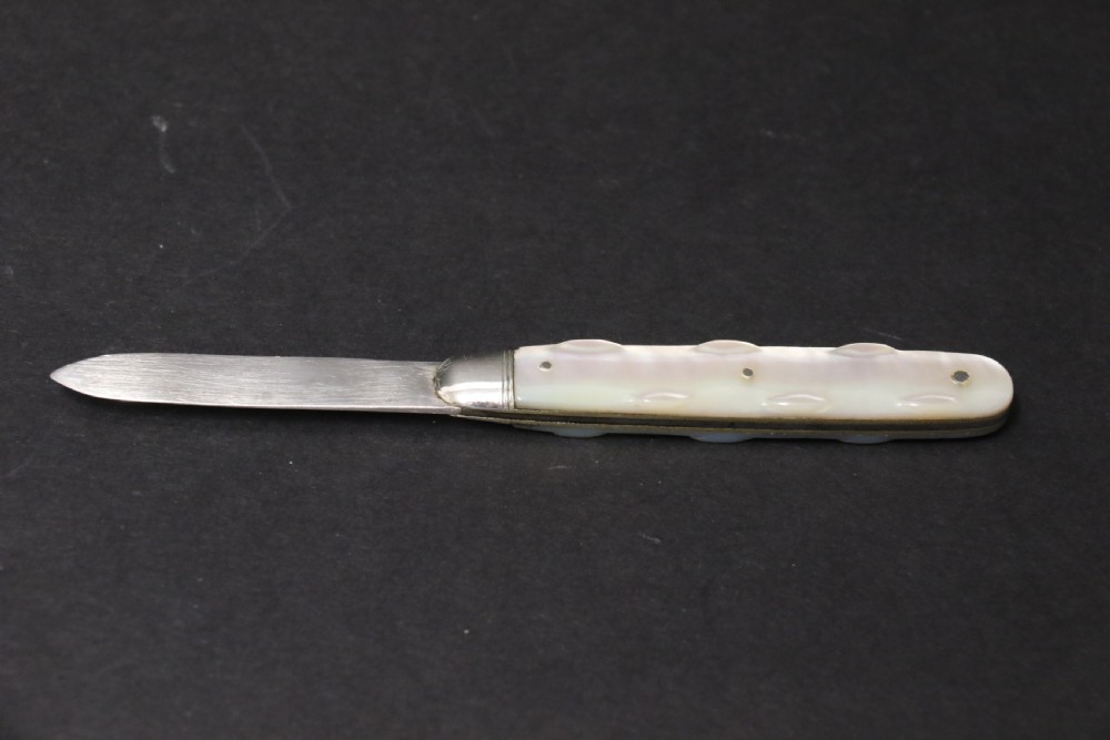 A George V sterling silver folding fruit knife featuring a hallmarked blade and a shaped mother of pearl handle with brass lining. View V