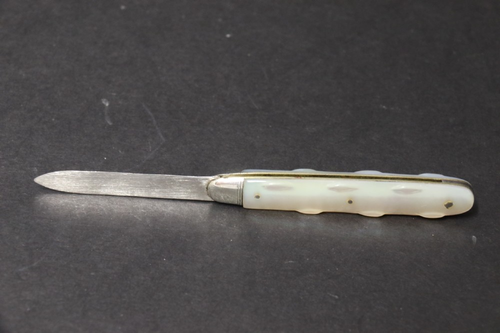 A George V sterling silver folding fruit knife featuring a hallmarked blade and a shaped mother of pearl handle with brass lining. View VI