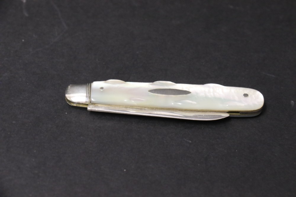 A George V sterling silver folding fruit knife featuring a hallmarked blade and a shaped mother of pearl handle with brass lining. View VII