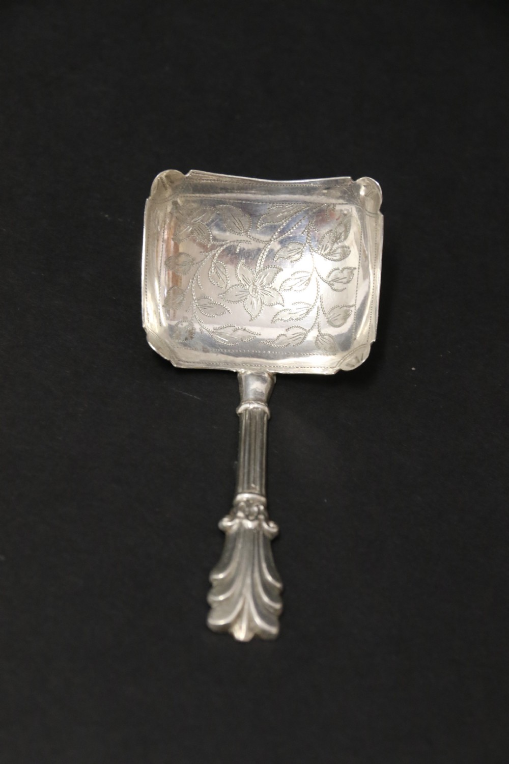 An antique Victorian silver caddy spoon featuring a rectangular bowl with bright-cut floral and leaf engraving and a decorative short handle. View IV