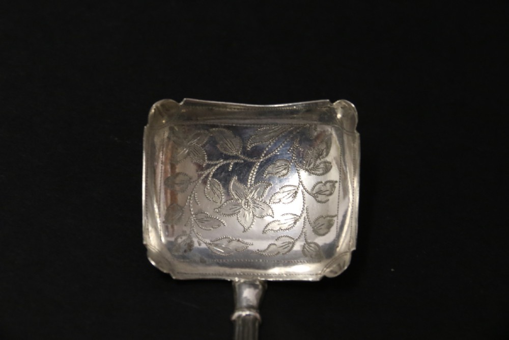 An antique Victorian silver caddy spoon featuring a rectangular bowl with bright-cut floral and leaf engraving and a decorative short handle. View V