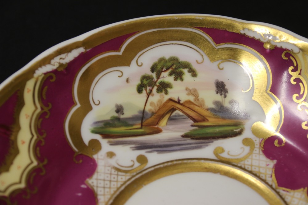 An early 19th-century English porcelain cabinet cup and saucer decorated with magenta borders, gold scrollwork gilding, and hand-painted miniature landscape vignettes. View III