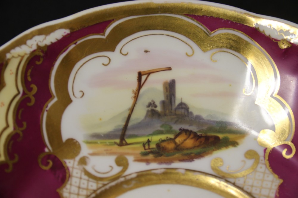 An early 19th-century English porcelain cabinet cup and saucer decorated with magenta borders, gold scrollwork gilding, and hand-painted miniature landscape vignettes. View VI