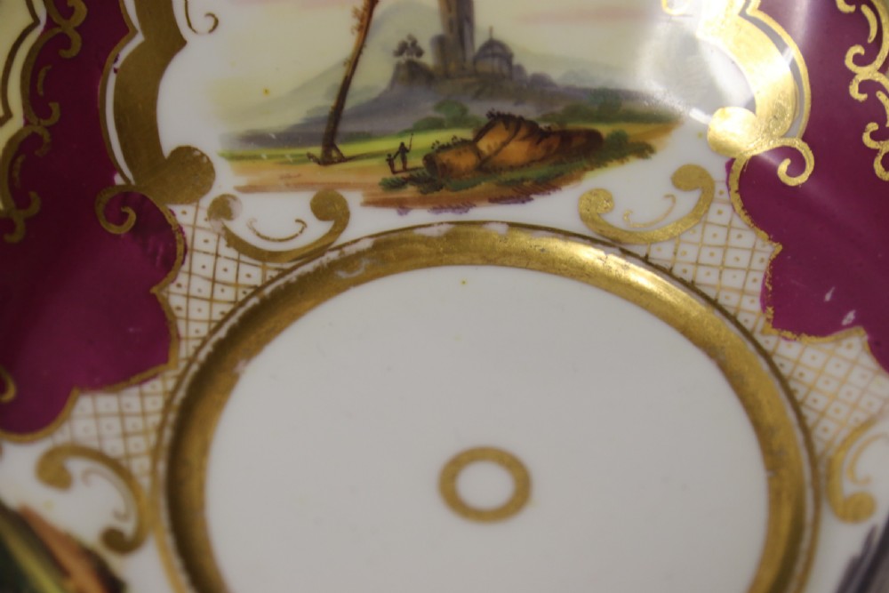 An early 19th-century English porcelain cabinet cup and saucer decorated with magenta borders, gold scrollwork gilding, and hand-painted miniature landscape vignettes. View VII
