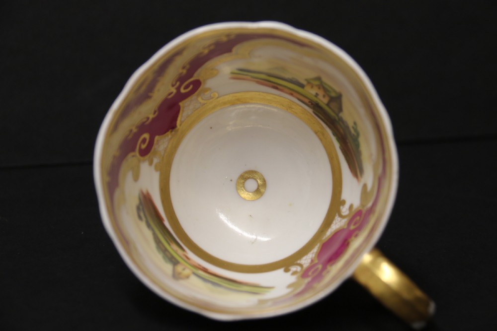 An early 19th-century English porcelain cabinet cup and saucer decorated with magenta borders, gold scrollwork gilding, and hand-painted miniature landscape vignettes. View X