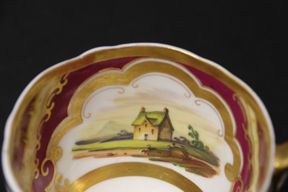 An early 19th-century English porcelain cabinet cup and saucer decorated with magenta borders, gold scrollwork gilding, and hand-painted miniature landscape vignettes. View XII