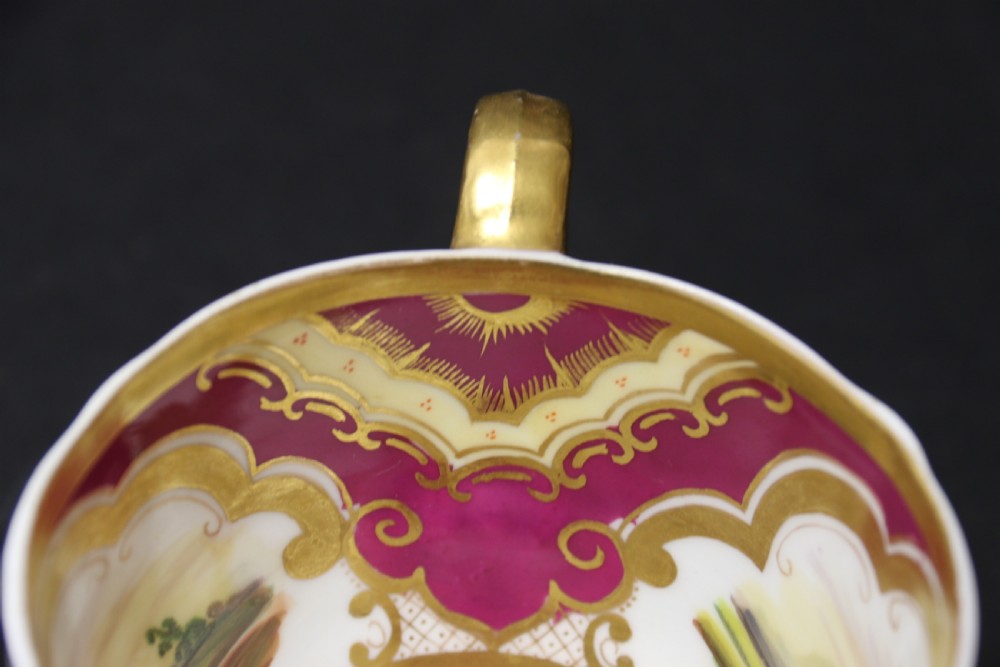 An early 19th-century English porcelain cabinet cup and saucer decorated with magenta borders, gold scrollwork gilding, and hand-painted miniature landscape vignettes. View XIII