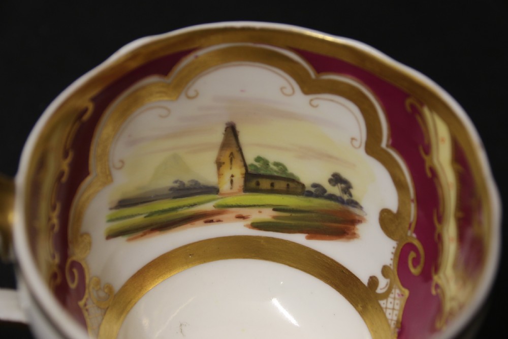 An early 19th-century English porcelain cabinet cup and saucer decorated with magenta borders, gold scrollwork gilding, and hand-painted miniature landscape vignettes. View XIV