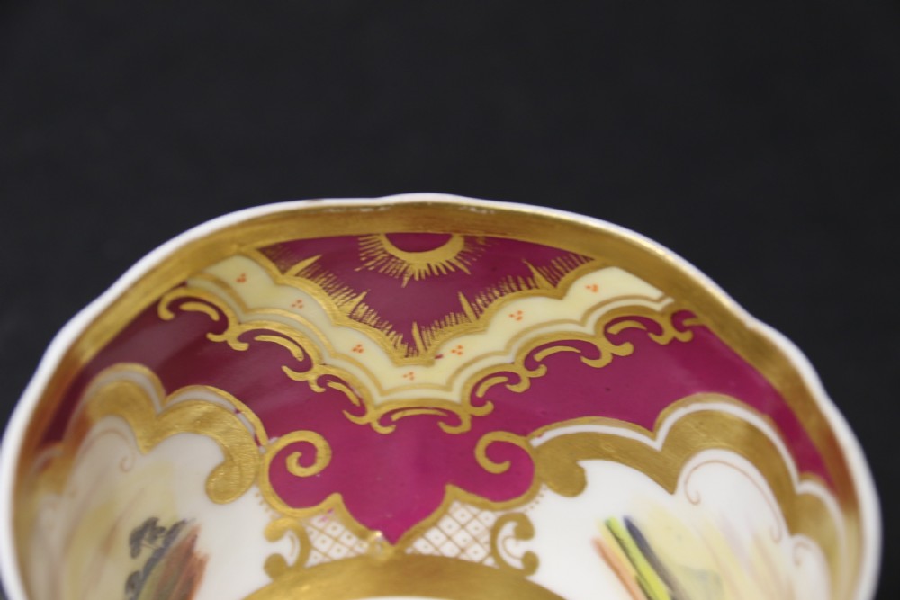 An early 19th-century English porcelain cabinet cup and saucer decorated with magenta borders, gold scrollwork gilding, and hand-painted miniature landscape vignettes. View XV