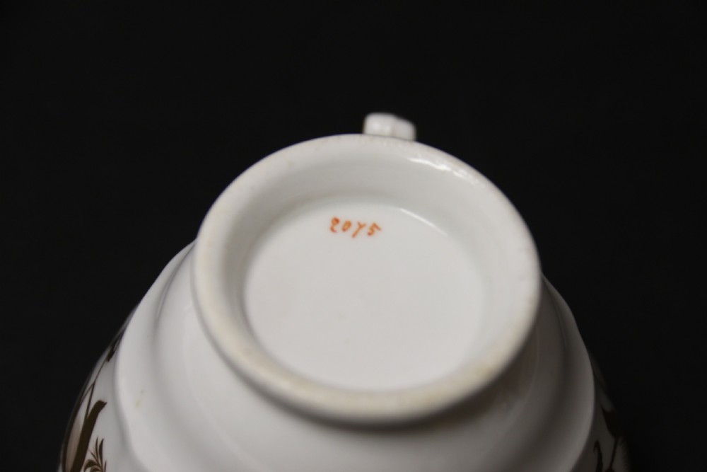 An early 19th-century English porcelain cabinet cup and saucer decorated with magenta borders, gold scrollwork gilding, and hand-painted miniature landscape vignettes. View XVI