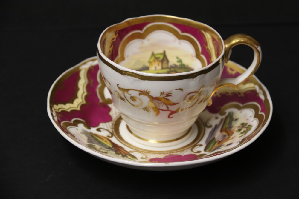 An early 19th-century English porcelain cabinet cup and saucer decorated with magenta borders, gold scrollwork gilding, and hand-painted miniature landscape vignettes. View XVII