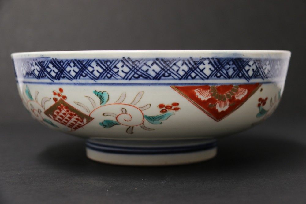 A round hand-painted Japanese porcelain bowl featuring underglaze blue geometric rim borders, iron-red floral panel motifs, and gilded details on a white background. View XI