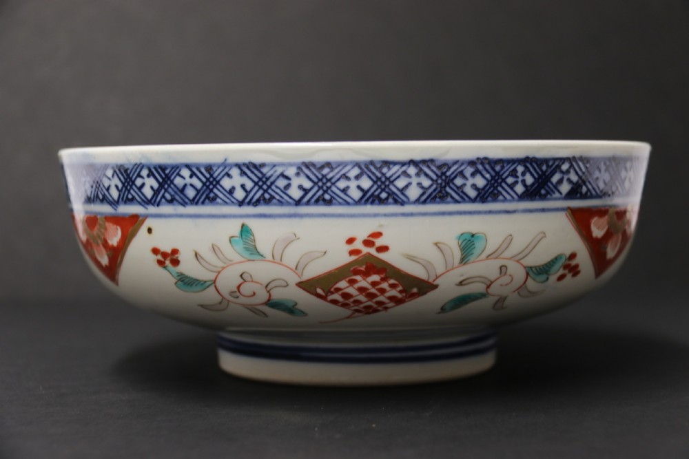 A round hand-painted Japanese porcelain bowl featuring underglaze blue geometric rim borders, iron-red floral panel motifs, and gilded details on a white background. View XII