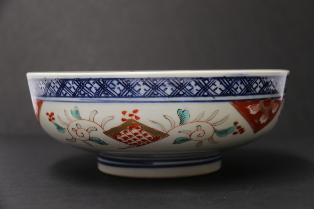A round hand-painted Japanese porcelain bowl featuring underglaze blue geometric rim borders, iron-red floral panel motifs, and gilded details on a white background. View XIV