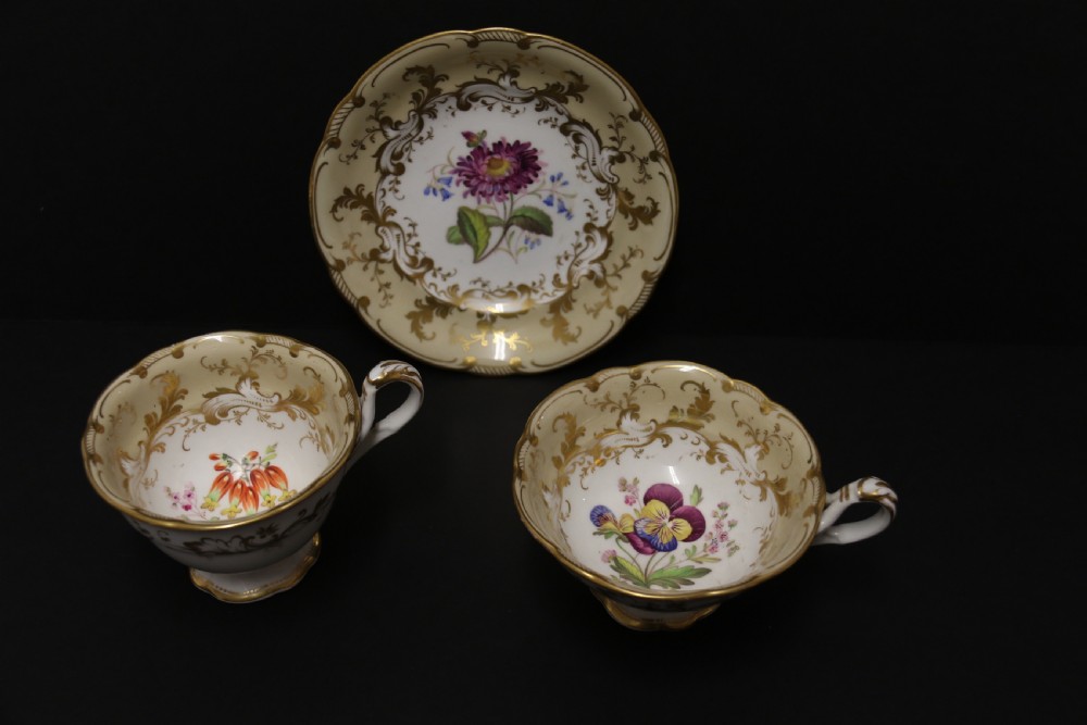 An early nineteenth-century Davenport porcelain cabinet trio comprising a teacup, coffee cup, and matching saucer decorated with hand-painted botanical flowers and gilded scrolling borders.
