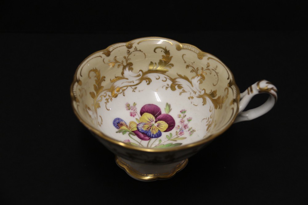 An early nineteenth-century Davenport porcelain cabinet trio comprising a teacup, coffee cup, and matching saucer decorated with hand-painted botanical flowers and gilded scrolling borders. View X