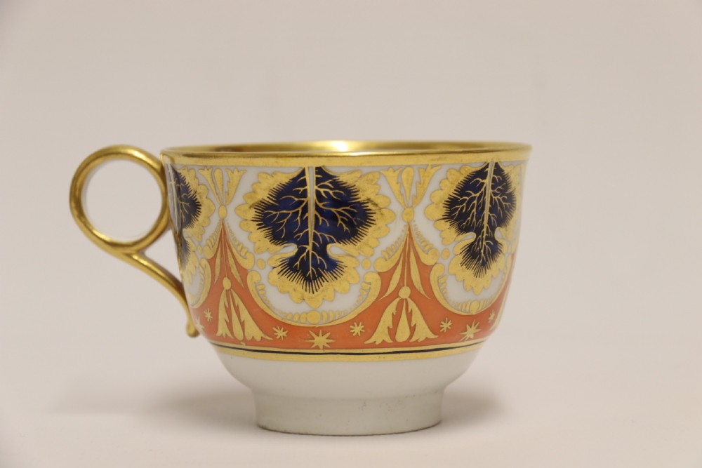 An early nineteenth-century porcelain cabinet cup and matching saucer decorated with orange panels, cobalt blue leaf motifs, and gold gilding. View X