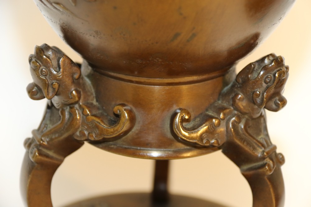 A pair of patinated Japanese Meiji period bronze vases featuring low-relief floral carving, curved scroll handles, and tripod legs resting on circular bases. View VI