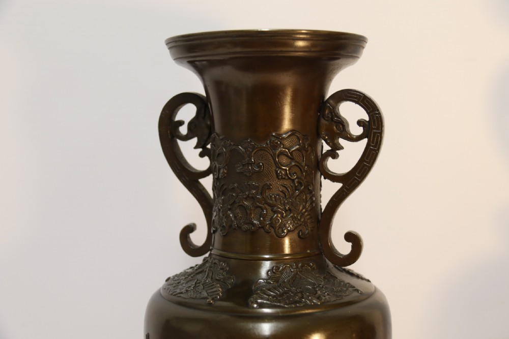 A pair of patinated Japanese Meiji period bronze vases featuring low-relief floral carving, curved scroll handles, and tripod legs resting on circular bases. View VIII