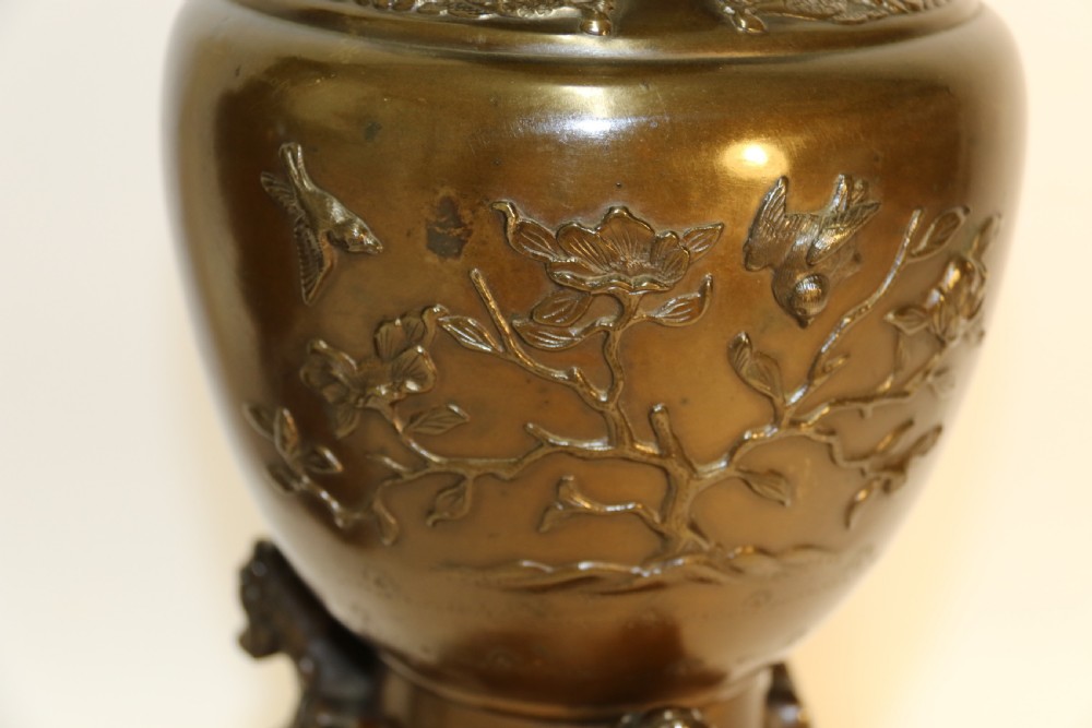 A pair of patinated Japanese Meiji period bronze vases featuring low-relief floral carving, curved scroll handles, and tripod legs resting on circular bases. View IX