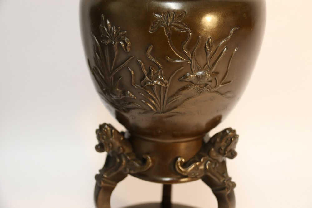 A pair of patinated Japanese Meiji period bronze vases featuring low-relief floral carving, curved scroll handles, and tripod legs resting on circular bases. View X