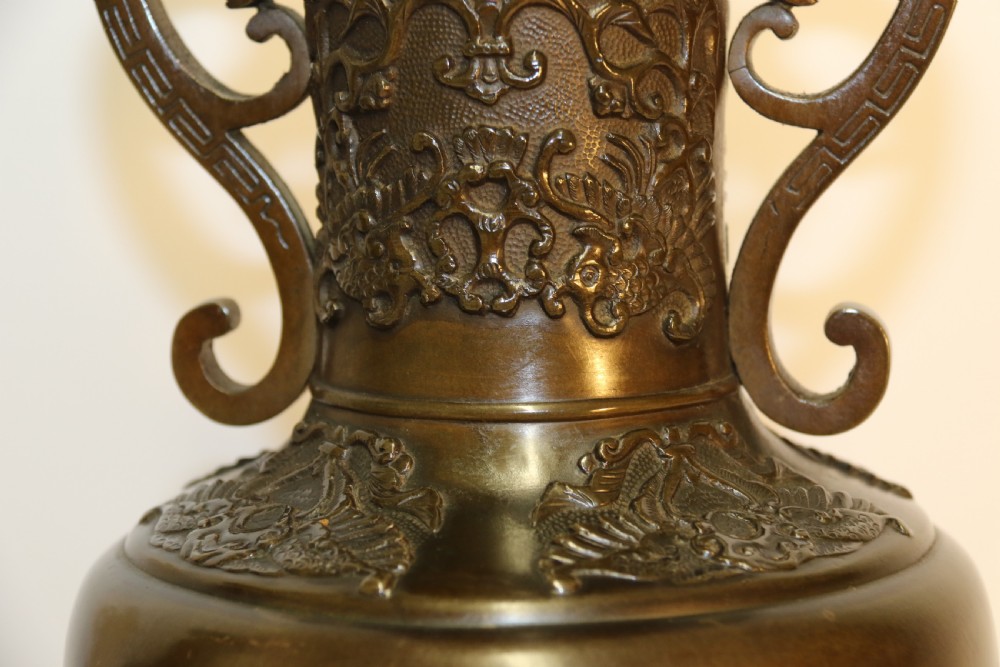 A pair of patinated Japanese Meiji period bronze vases featuring low-relief floral carving, curved scroll handles, and tripod legs resting on circular bases. View XI