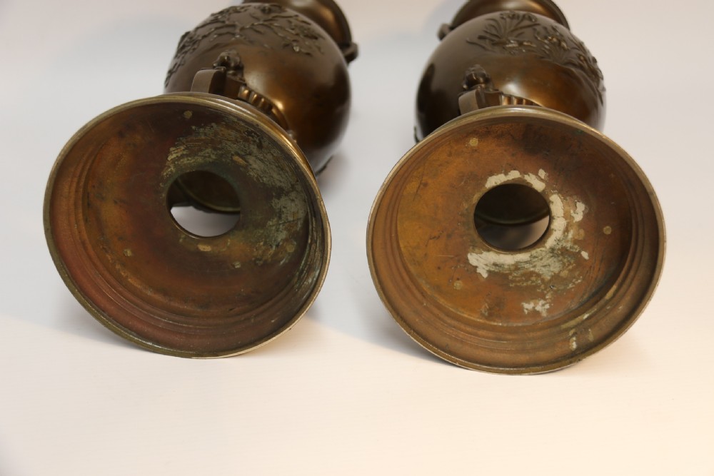 A pair of patinated Japanese Meiji period bronze vases featuring low-relief floral carving, curved scroll handles, and tripod legs resting on circular bases. View XII