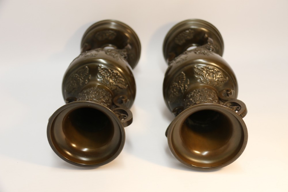 A pair of patinated Japanese Meiji period bronze vases featuring low-relief floral carving, curved scroll handles, and tripod legs resting on circular bases. View XIII