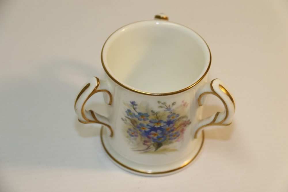 A white miniature porcelain loving cup featuring twin gilded scroll handles and a hand-painted blue floral spray. View VIII