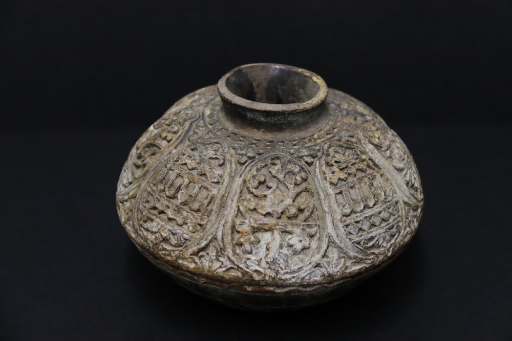 A squat, rounded antique Indian earthenware vase featuring deeply incised floral and arch motifs across its upper body.