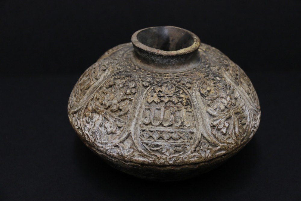 A squat, rounded antique Indian earthenware vase featuring deeply incised floral and arch motifs across its upper body. View II