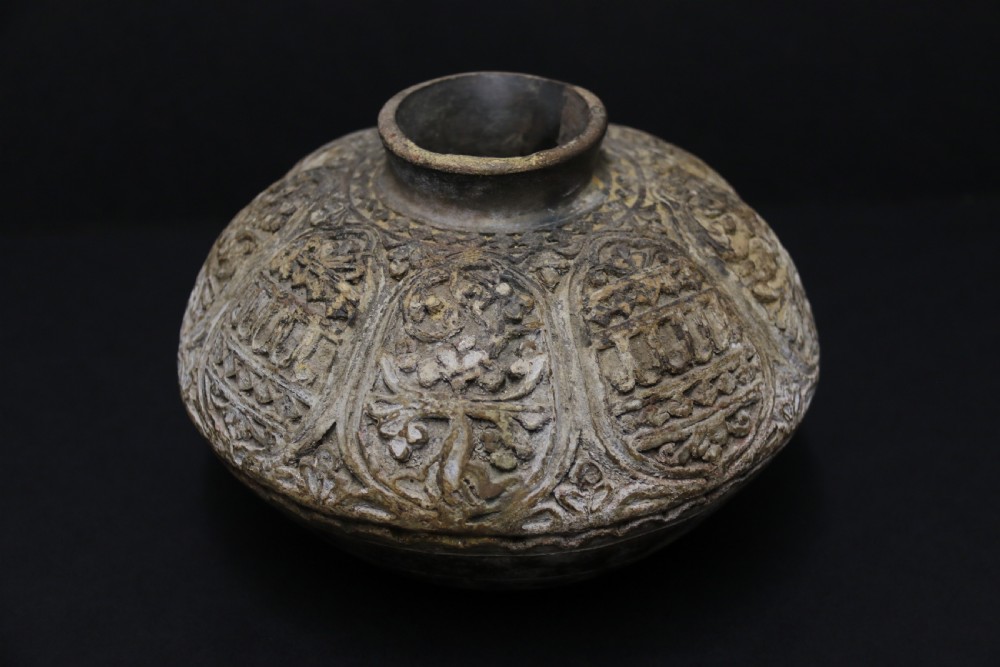 A squat, rounded antique Indian earthenware vase featuring deeply incised floral and arch motifs across its upper body. View III