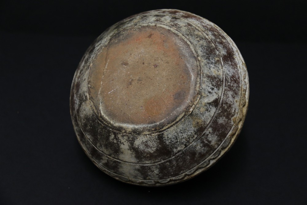 A squat, rounded antique Indian earthenware vase featuring deeply incised floral and arch motifs across its upper body. View V