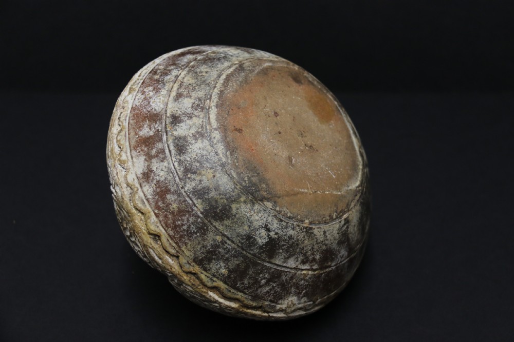 A squat, rounded antique Indian earthenware vase featuring deeply incised floral and arch motifs across its upper body. View VII