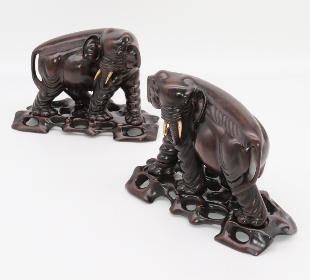 A pair of hand-carved dark hardwood elephant figures standing on pierced wooden bases with exposed tusks. View XXVIII