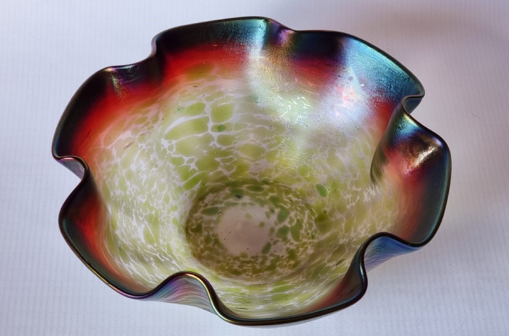 A hand-blown glass bowl featuring an undulating ruffled rim and a shimmering iridescent finish in shades of green, purple, and red. View V