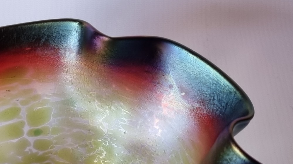 A hand-blown glass bowl featuring an undulating ruffled rim and a shimmering iridescent finish in shades of green, purple, and red. View VII