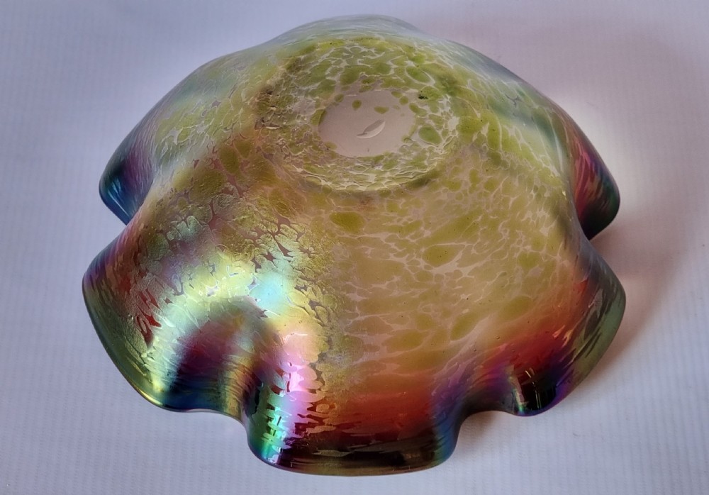 A hand-blown glass bowl featuring an undulating ruffled rim and a shimmering iridescent finish in shades of green, purple, and red. View VIII