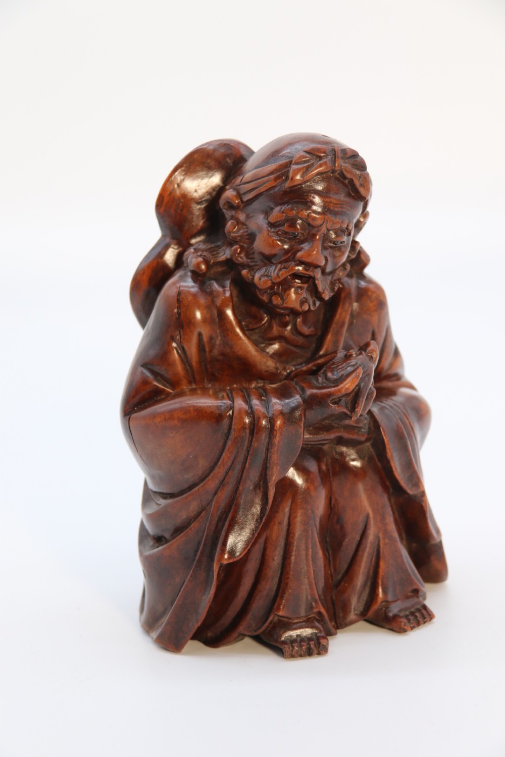 A fine Japanese carved hardwood mid 19th century Okimono of a seated man holding a bat. View II