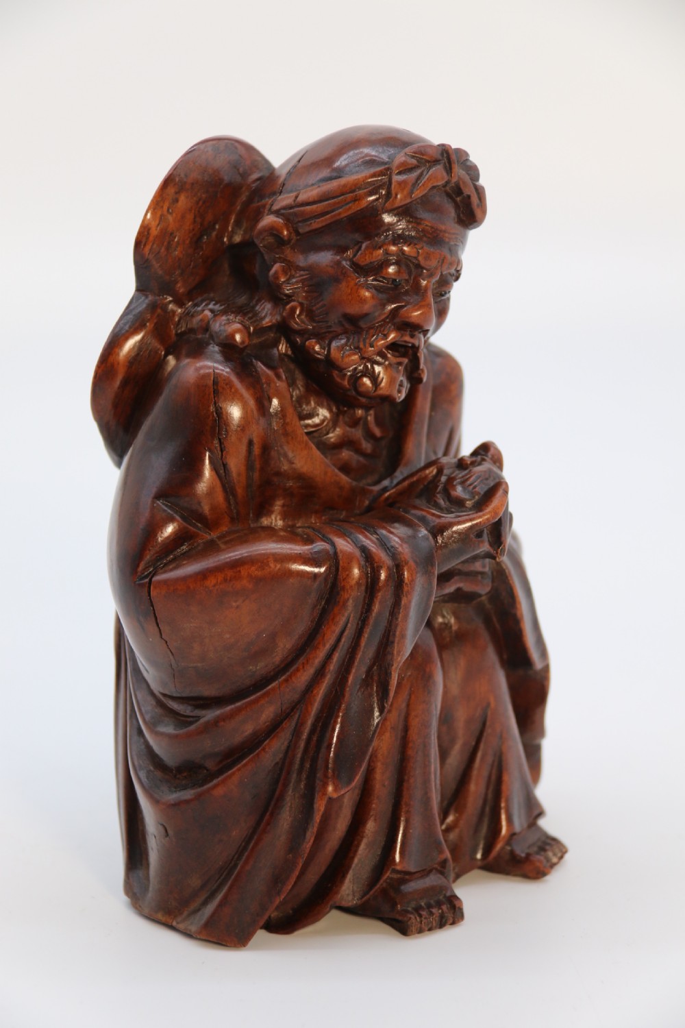 A fine Japanese carved hardwood mid 19th century Okimono of a seated man holding a bat. View III